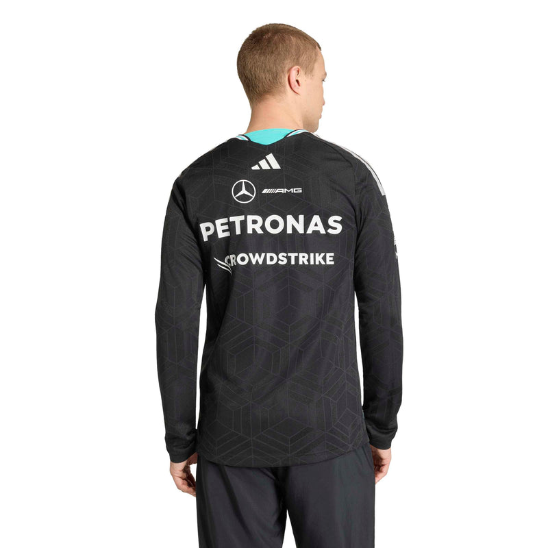 adidas man viewed from the back wearing a black long-sleeve Adidas Mercedes-Benz racing jersey with white sponsor logos including Petronas and CrowdStrike, on a white studio background.
